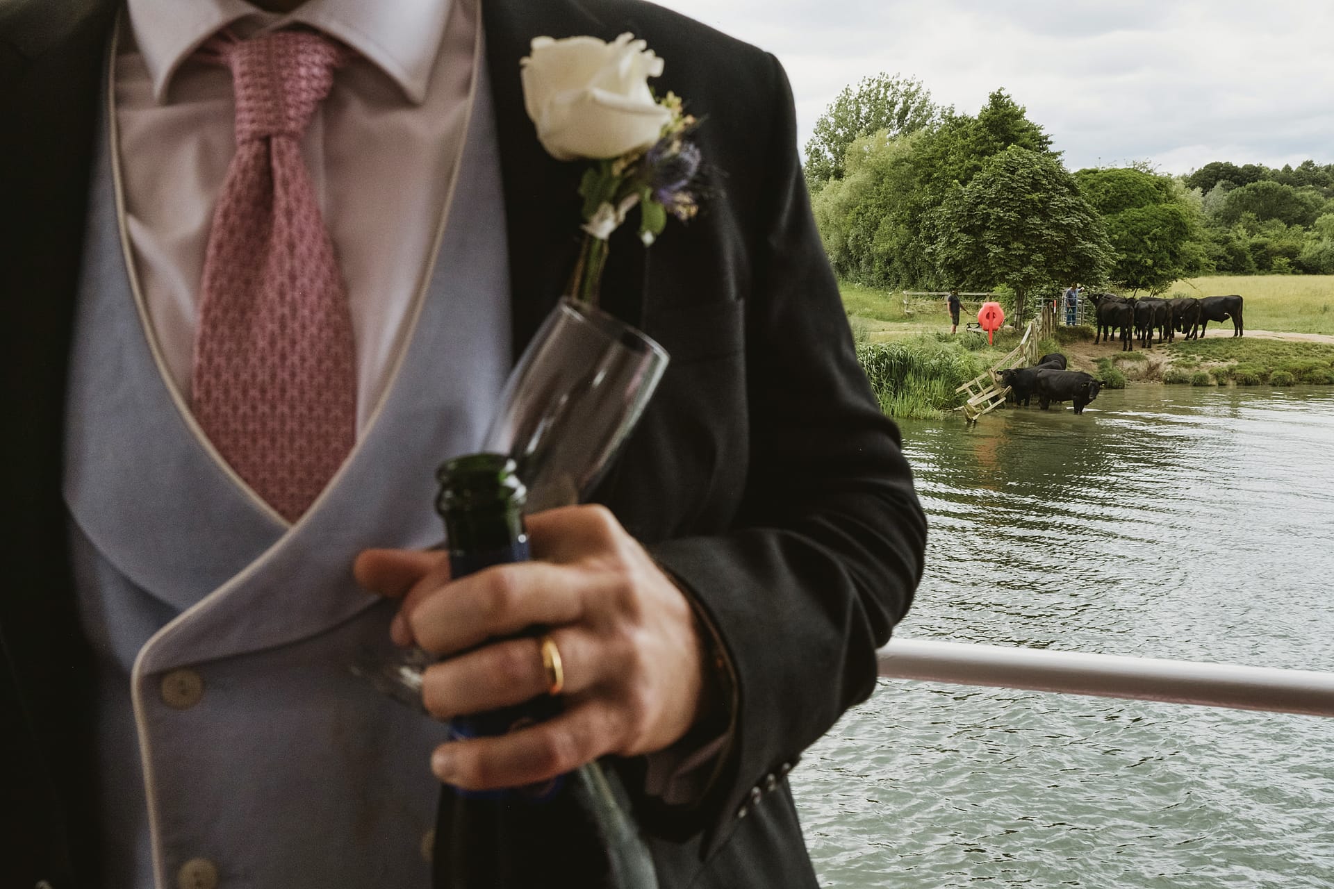 Man in suit holding champagne bottle near river.