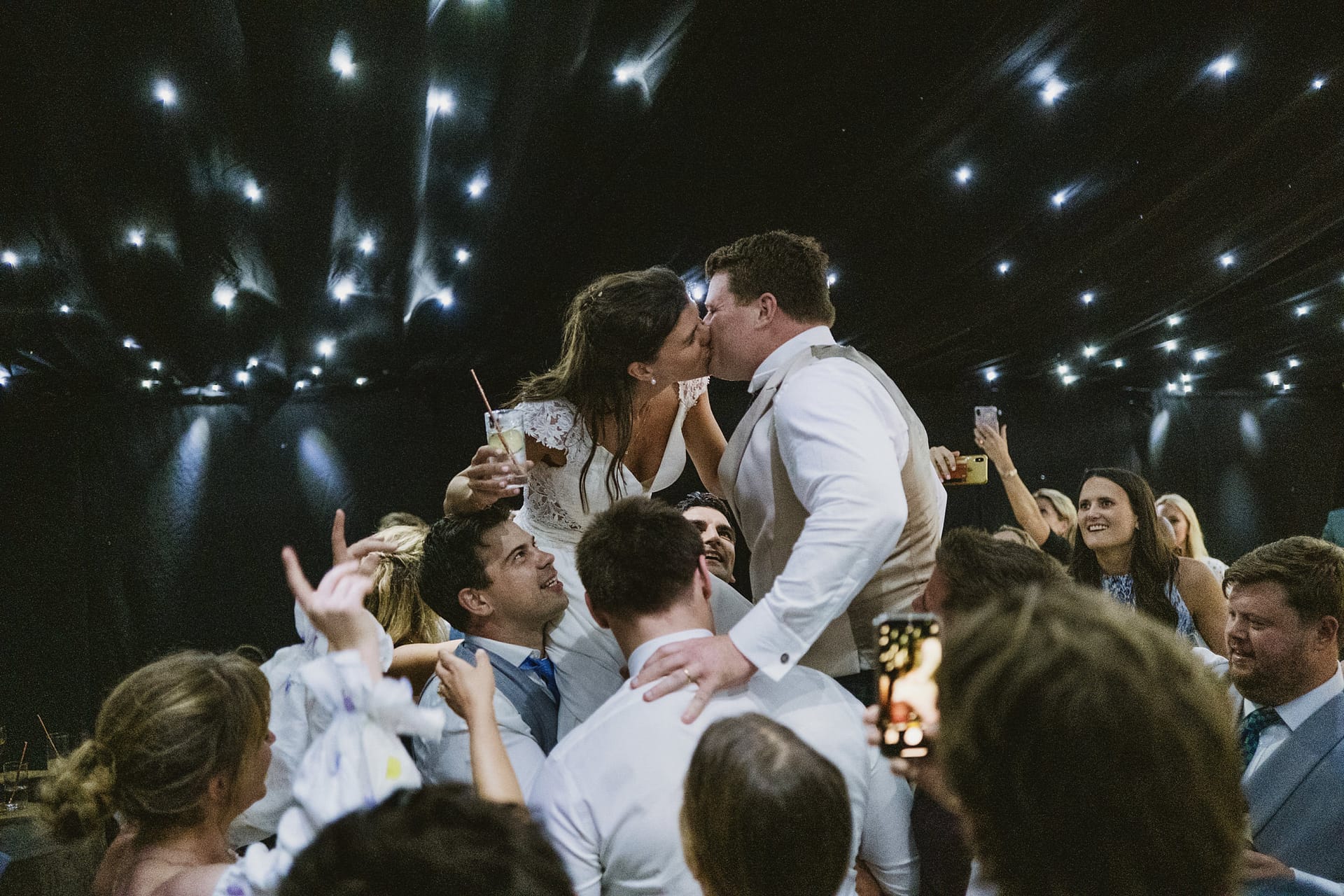 Newlyweds kiss on shoulders at wedding reception.