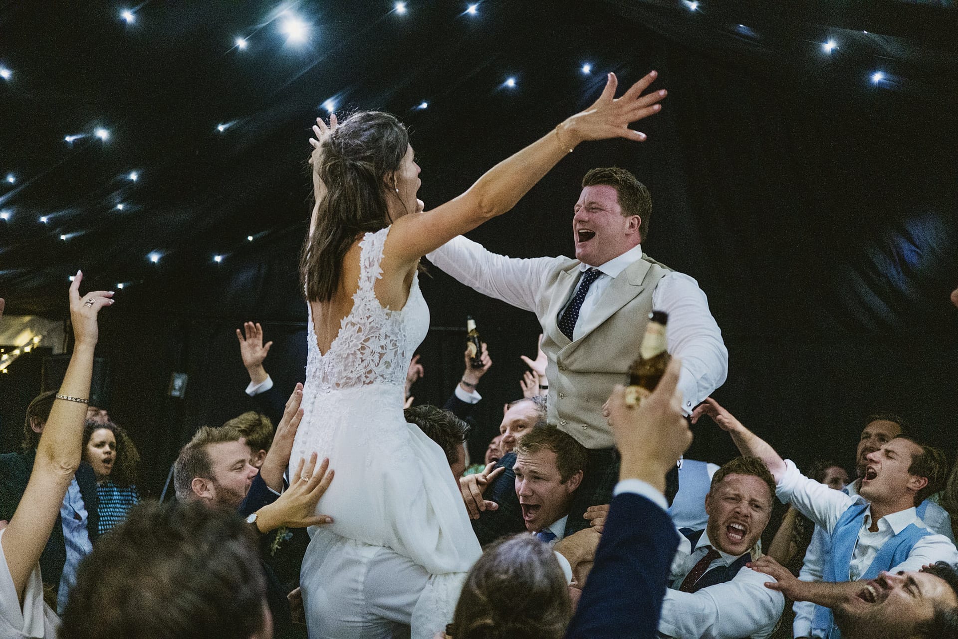 Wedding guests lifting bride and groom on dance floor.