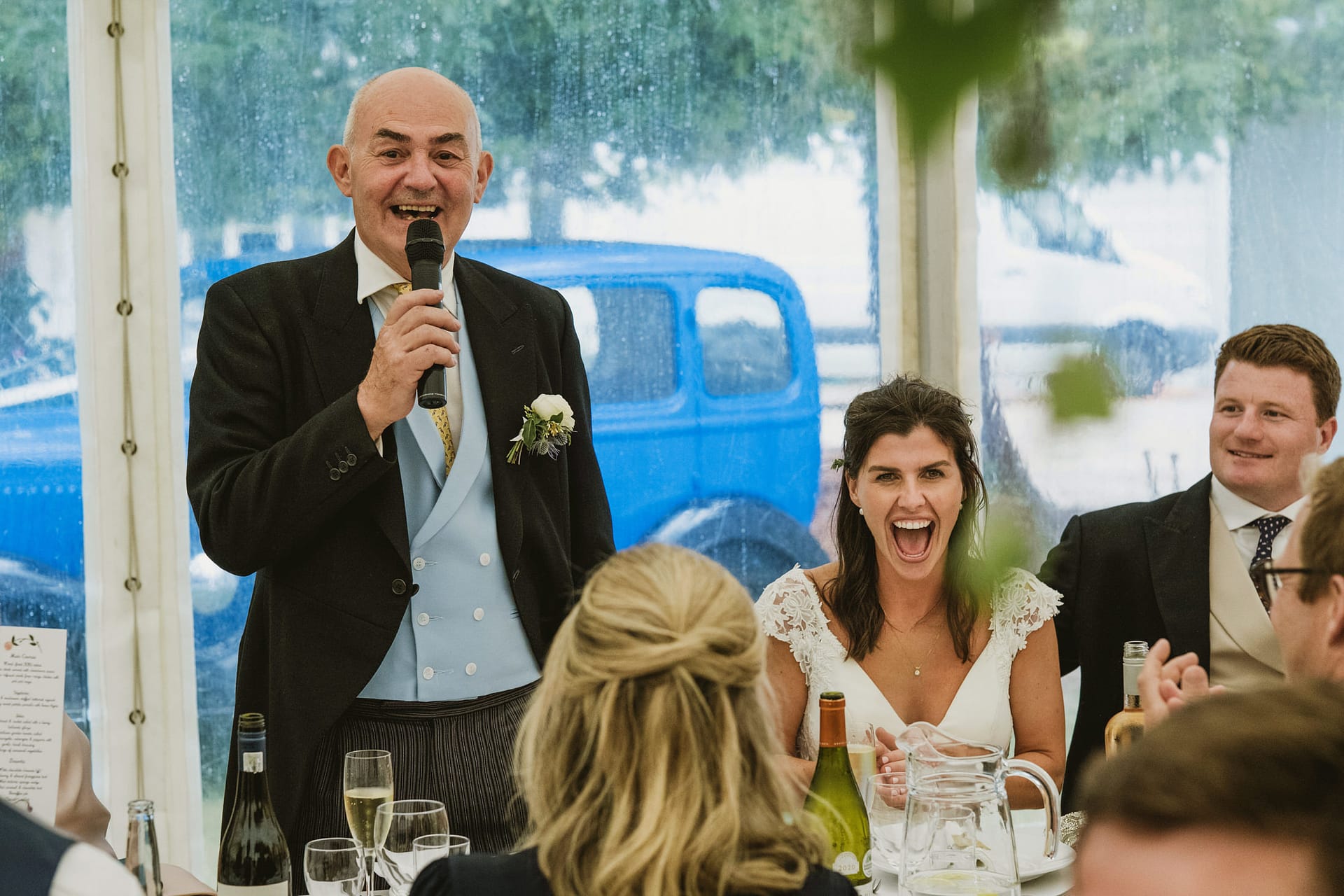 Man giving wedding speech with guests laughing.