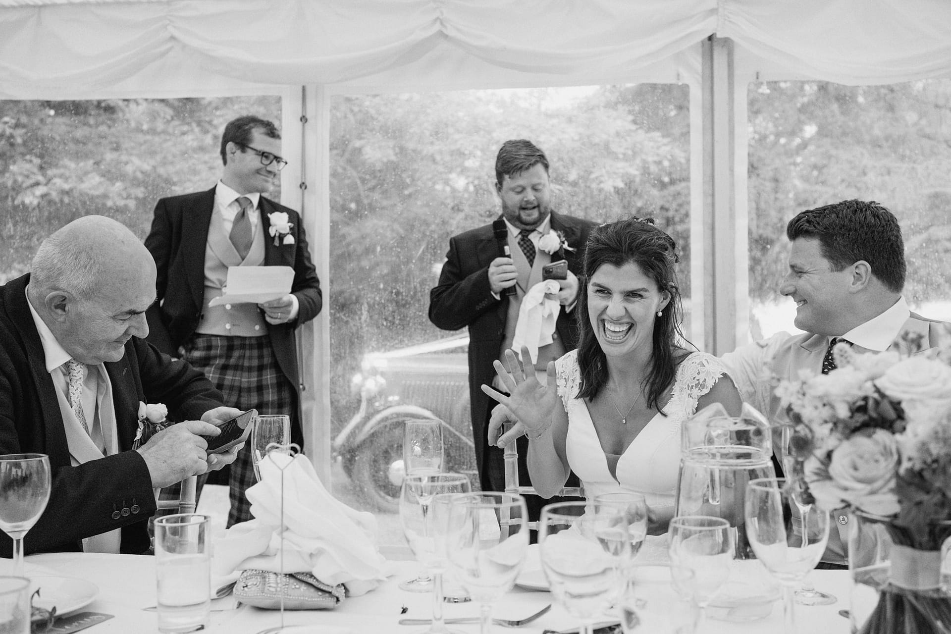 Wedding speech with smiling bride under marquee.