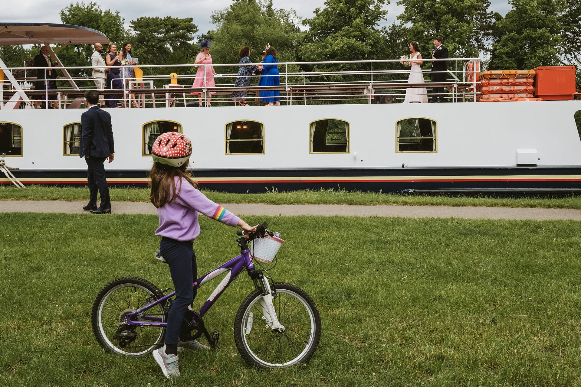 Buckinghamshire documentary wedding photography. Girl on bike watches people on moored boat.