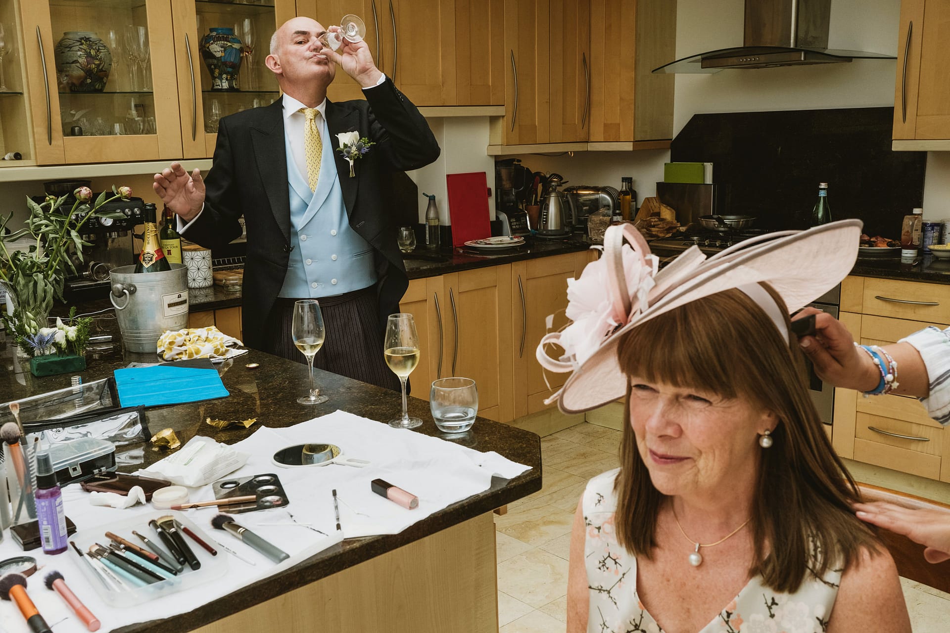 Father of the bride has a quick drink whilst the Mother of the Bride has her hair finished in their home in Buckinghamshire