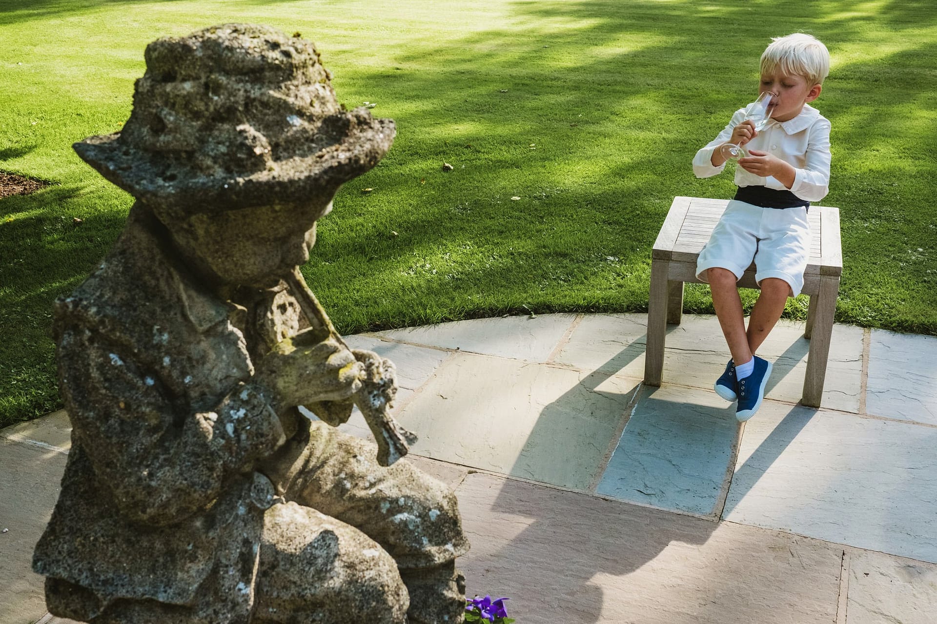 Documentary wedding photography, page boy drinking water in symmetry with stone boy playing a flute
