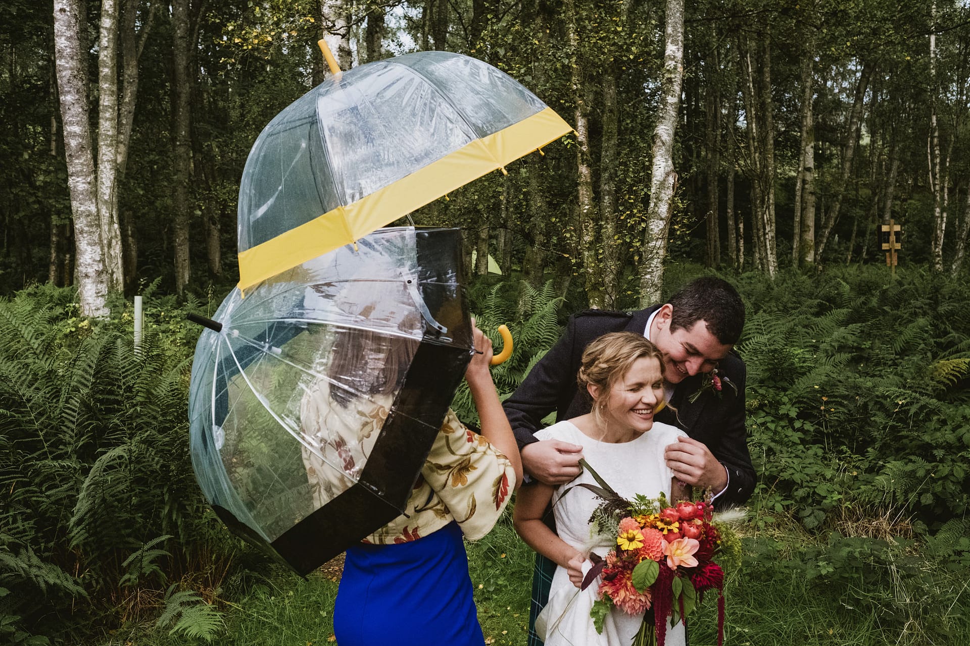 Comrie Croft Wedding Photography, bride and groom waiting, wedding guest helping with umbrellas