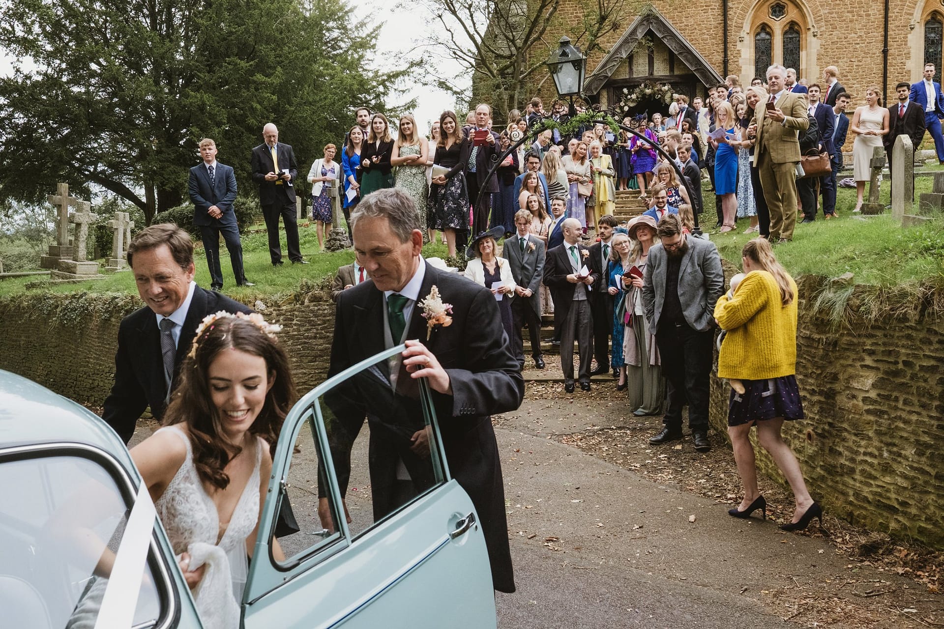 bride and groom leaving in wedding car with all guests watching