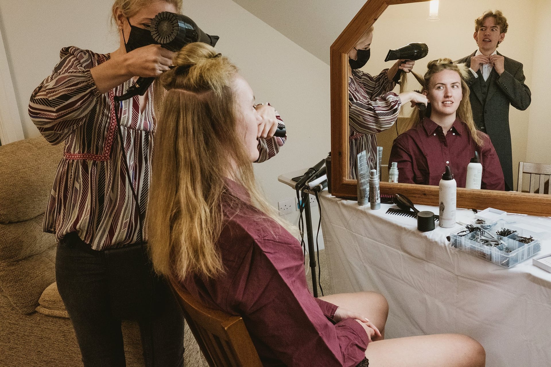 bridesmaid having her hair done whilst family member prepares in background tying his tie