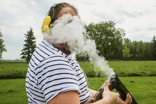 During a round of clay pigeon shooting a wedding guest's face becomes momentarily hidden by smoke as he reloads his shotgun. Documentary wedding photograph by York Place Studios