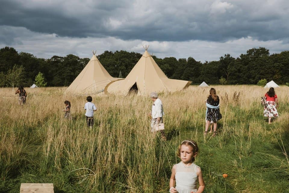 Documentary / reportage wedding photograph - guests appear to look for something around a tipi